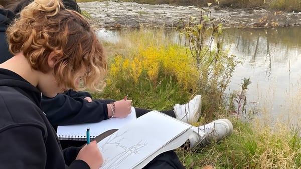 Una persona escribe en un cuaderno junto a un estanque en la naturaleza en el terreno de la Henry Wise Wood High School.