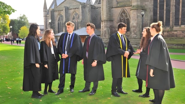 Un grupo de estudiantes en togas de graduación está frente a un gran edificio de piedra en el campus de la Hereford Cathedral School.