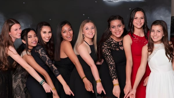 Un grupo de jóvenes mujeres en ropa formal posan frente a un fondo oscuro con una media luna y estrellas en el campus de la Heritage Christian School.