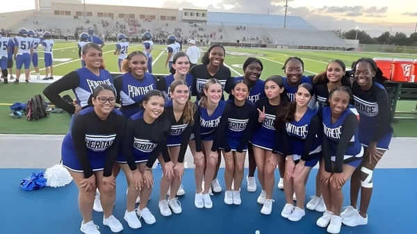Un grupo de animadoras en uniformes azules y blancos está en el campo deportivo de la Heritage High School.