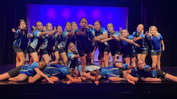 Estudiantes de la Hervey Bay State High School realizan una pieza de danza en un escenario con fondo azul.