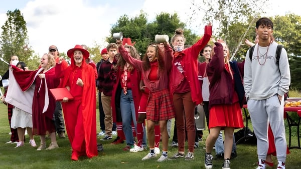 Un grupo de estudiantes de la High Mowing School lleva trajes rojos y sostiene banderas en un prado al aire libre.