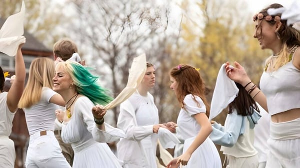 Un grupo de jóvenes mujeres en vestidos blancos está de pie en un campo en la naturaleza en el campus de la High Mowing School.
