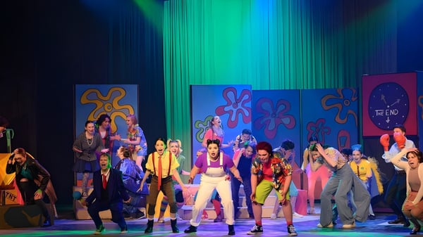 Estudiantes de la Highland Secondary School realizan una colorida actuación en el escenario con un fondo psicodélico.