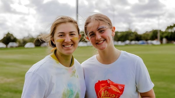 Dos estudiantes femeninas de Highlands Christian College posan sonriendo al aire libre frente a árboles y un cielo nublado.