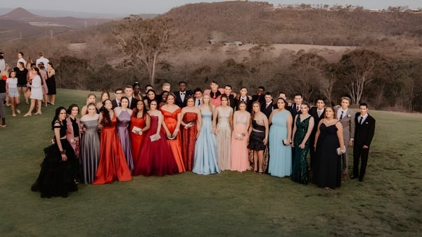 Un gran grupo de estudiantes de Highlands Christian College está de pie en un prado frente a un paisaje montañoso.