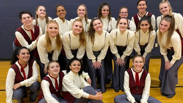 Un grupo de estudiantes de la Higley High School posan en el gimnasio con uniformes de animadoras uniformes.