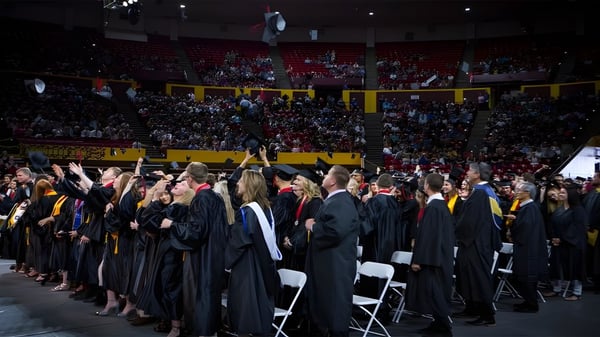 Los graduados del Higley Unified School District están en túnicas negras durante la ceremonia de graduación en un auditorio lleno.
