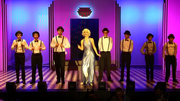 Un grupo de estudiantes de Hillcrest Christian College está juntos en una actuación en el escenario con iluminación colorida.