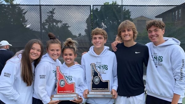 Un grupo de estudiantes de la Hillcrest High School posan juntos con premios al aire libre frente a un área cercada con árboles.