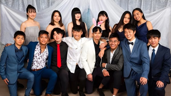 Un grupo de estudiantes de la Hillmorton High School posan con ropa formal frente a cortinas blancas.