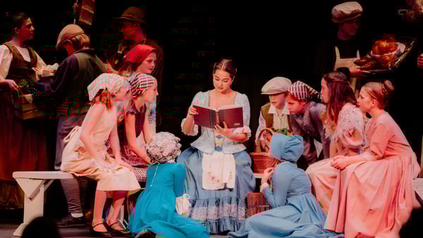 Estudiantes de la Hilton Head Preparatory School están en trajes históricos en un escenario y representan una obra de teatro.