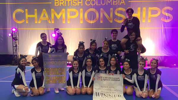 Un grupo de jóvenes gimnastas de la H.J. Cambie Secondary School posan juntos en el escenario frente a un banner de los Campeonatos de Columbia Británica.