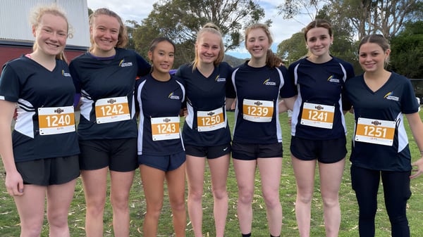 Un grupo de jóvenes atletas se encuentra en el campus de la Hobart City High School frente a un fondo boscoso.