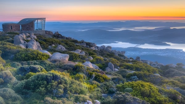 El edificio de vidrio en una roca ofrece una vista de montañas y lagos en el terreno del Hobart College al atardecer.