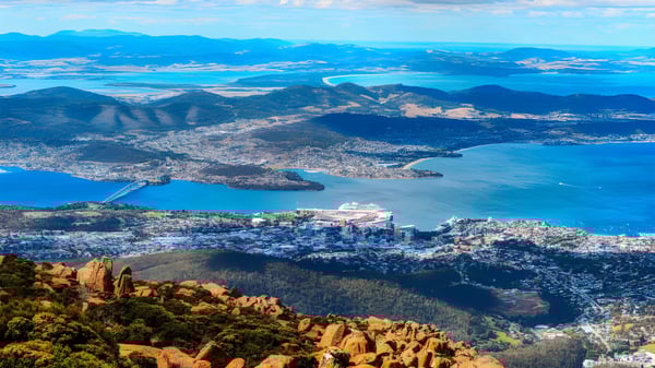 Toma aérea de una ciudad costera con montañas y agua cerca de la Hobart City High School.
