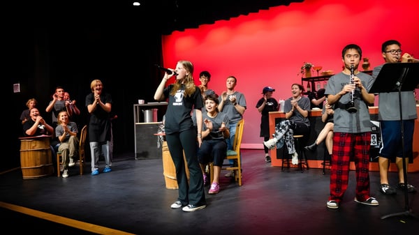Estudiantes de la Holderness School están con instrumentos musicales en un escenario frente a un fondo rojo.