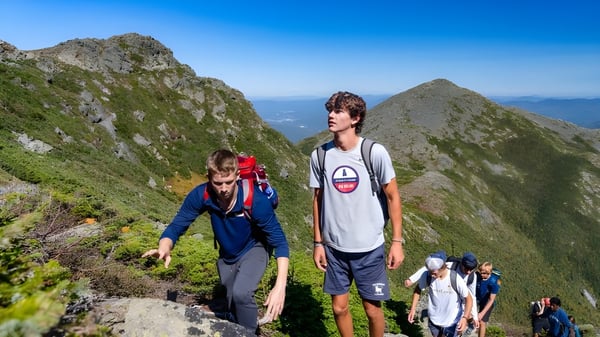 Un grupo de estudiantes de la Holderness School camina por un sendero montañoso con cielo azul claro.
