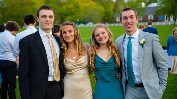 Cuatro estudiantes de la Holderness School posan en ropa formal juntos al aire libre frente a árboles y un prado.