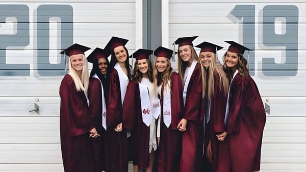 Un grupo de graduados con togas rojas se encuentra frente a una pared con el año 2019 en el campus de Holland Christian Schools.