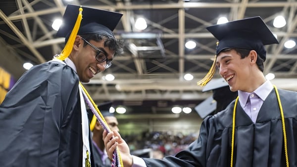 Dos graduados conversan durante una ceremonia de graduación en el campus de la Holy Cross High School.