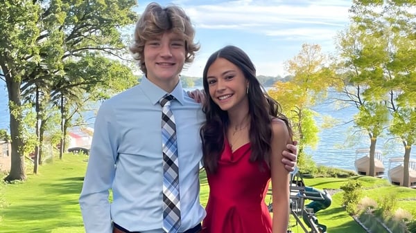 Una joven pareja está junta en un paisaje verde fuera de la Holy Family Catholic High School.