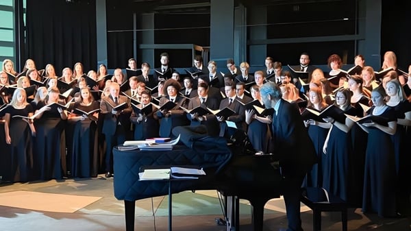 El coro de la Holy Family Catholic High School está en túnicas negras y azules en el escenario frente a un piano.