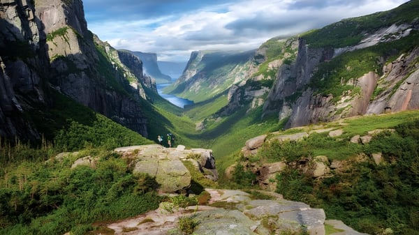 Paisaje montañoso con acantilados empinados y un valle verde bajo un cielo nublado cerca de la Holy Heart of Mary High School.