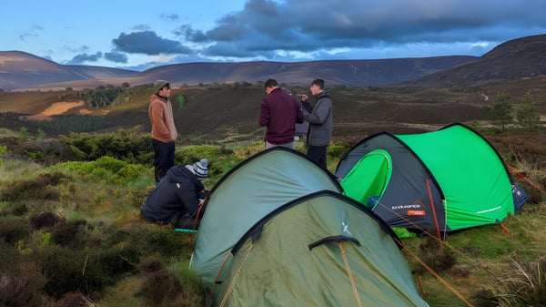 Un grupo de alumnos de la Holy Rood High School acampando en un paisaje montañoso con tiendas de campaña en primer plano.