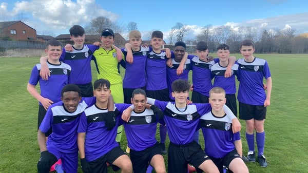 Alumnos de la Holy Rood High School están de pie en sus camisetas moradas y amarillas en el campo de fútbol.