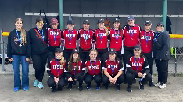 Un grupo de alumnas y alumnos en camisetas rojas con la inscripción HSH están en el campo de deportes de la Holy Spirit High School.