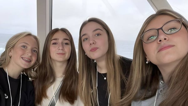 Cuatro alumnas de la Holy Trinity High School posan frente a una ventana con vista al cielo nublado.