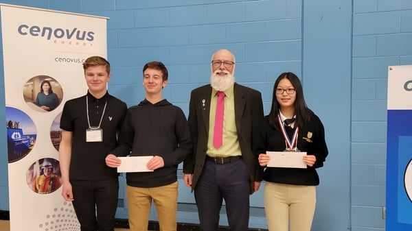Cuatro personas están frente a una pared azul con el logo de Cenovus en un evento de la Holy Trinity High School.