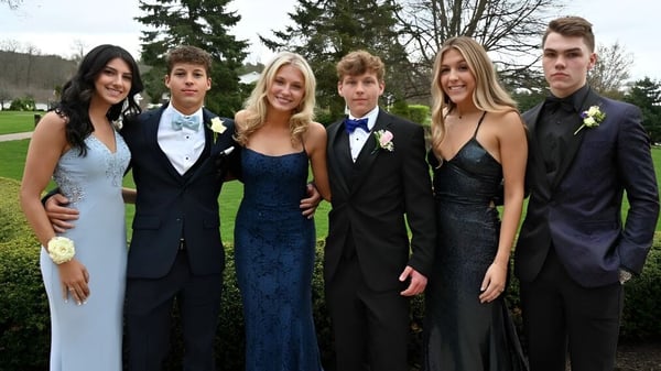 Un grupo de estudiantes de Honourable W.C. Kennedy Collegiate posan juntos en un área exterior parecida a un parque con árboles.