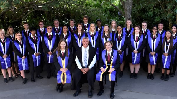 Un grupo de graduados de Howick College está juntos en ropa académica en el área verde.