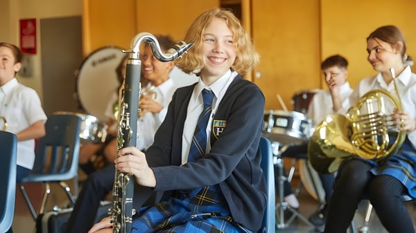 Un estudiante del Hudson College toca entusiasmado un instrumento musical en la clase de música con otros estudiantes de fondo.