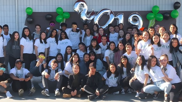 Un grupo de estudiantes se encuentra frente a un banner con el año 2019 en el campus de la Hugh McRoberts Secondary School.