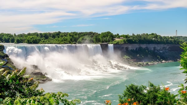 Una cascada fluye sobre un acantilado, rodeada de vegetación verde, visible cerca de la École Secondaire Hugh McRoberts Secondary School.