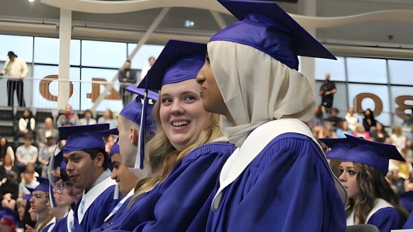 Un grupo de graduados de la Hunting Hills High School lleva togas y birretes morados en un auditorio lleno.