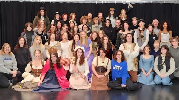 Un gran grupo de mujeres posando juntas en el escenario de la Hunting Hills High School frente a una cortina negra.