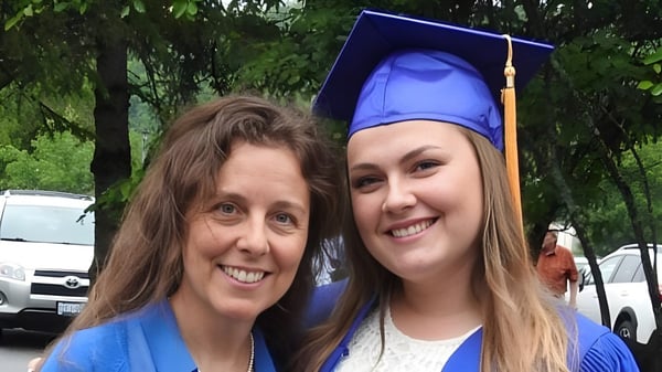 Dos mujeres, una con gorra de graduación, están juntas frente a un fondo boscoso en el campus de la Huntsville High School.