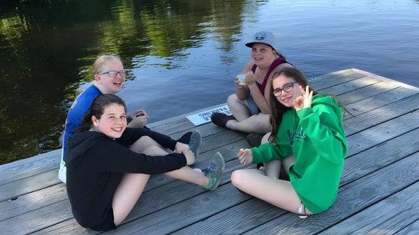 Un grupo de jóvenes mujeres está sentada en un muelle de madera junto al lago en el terreno de la Huntsville High School.