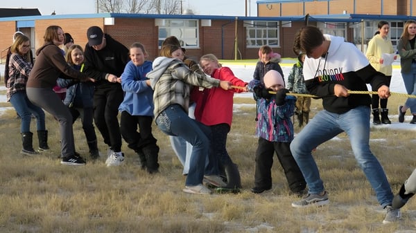 Estudiantes de la Huntsville School participan en una actividad en equipo al aire libre en un campo junto a un edificio de ladrillo.