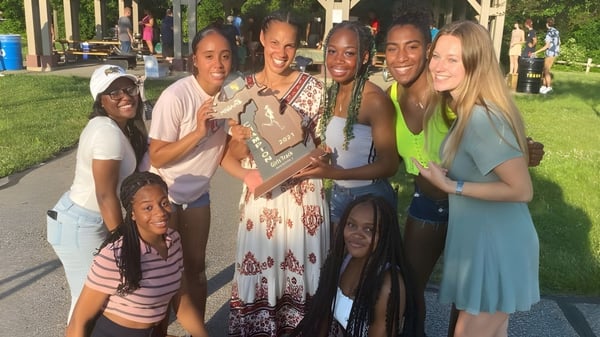 Estudiantes de la Huron High School sostienen juntos un trofeo al aire libre y están frente a edificios y árboles.