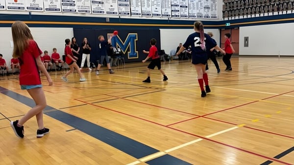 Estudiantes juegan baloncesto en la cancha de madera con el gran logo M en el Huron-Perth Catholic District School Board.
