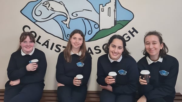 Cuatro estudiantes en uniformes escolares están frente a un mural con un castillo y paisaje en el campus del Iascaigh College.