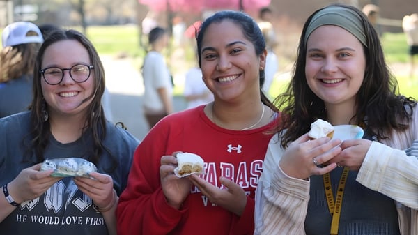Tres estudiantes sonrientes están juntas en el área exterior de Illinois Eastern Community Colleges con árboles y edificios de fondo.