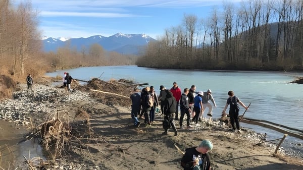 Un grupo de estudiantes de la Imagine High Integrated Arts and Technology Secondary School camina junto a un río por un camino fangoso con montañas nevadas al fondo.