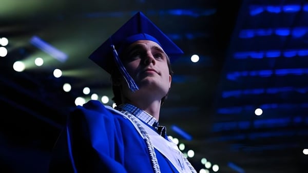 Una persona en toga y birrete azules está de pie en la luz tenue en el campus de la IMG Academy.
