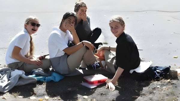 Un grupo de alumnas y alumnos de la Immaculata Regional School está sentado en la playa y disfrutando juntos de su tiempo libre al aire libre.